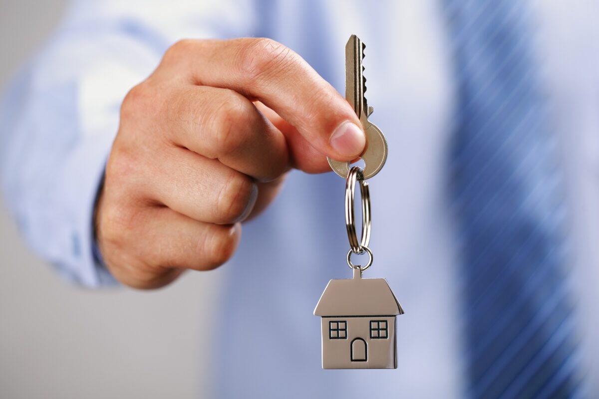 Property agent Holding out house keys on a house shaped keychain